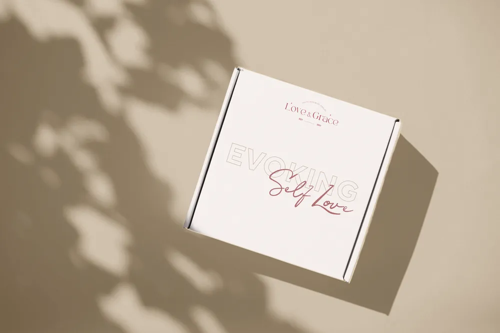 A Love & Grace gift box printed with “Evoking Self Love”, in dappled shade.