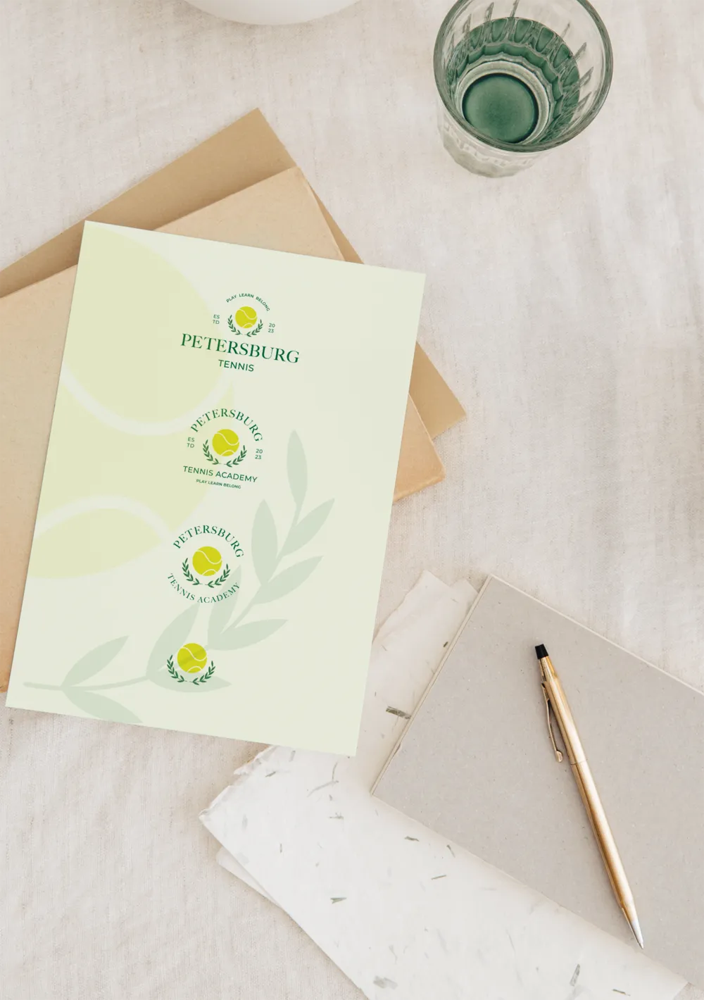 Stationery printed with the Petersburg Tennis Academy crest, beside a pen and a glass of water.