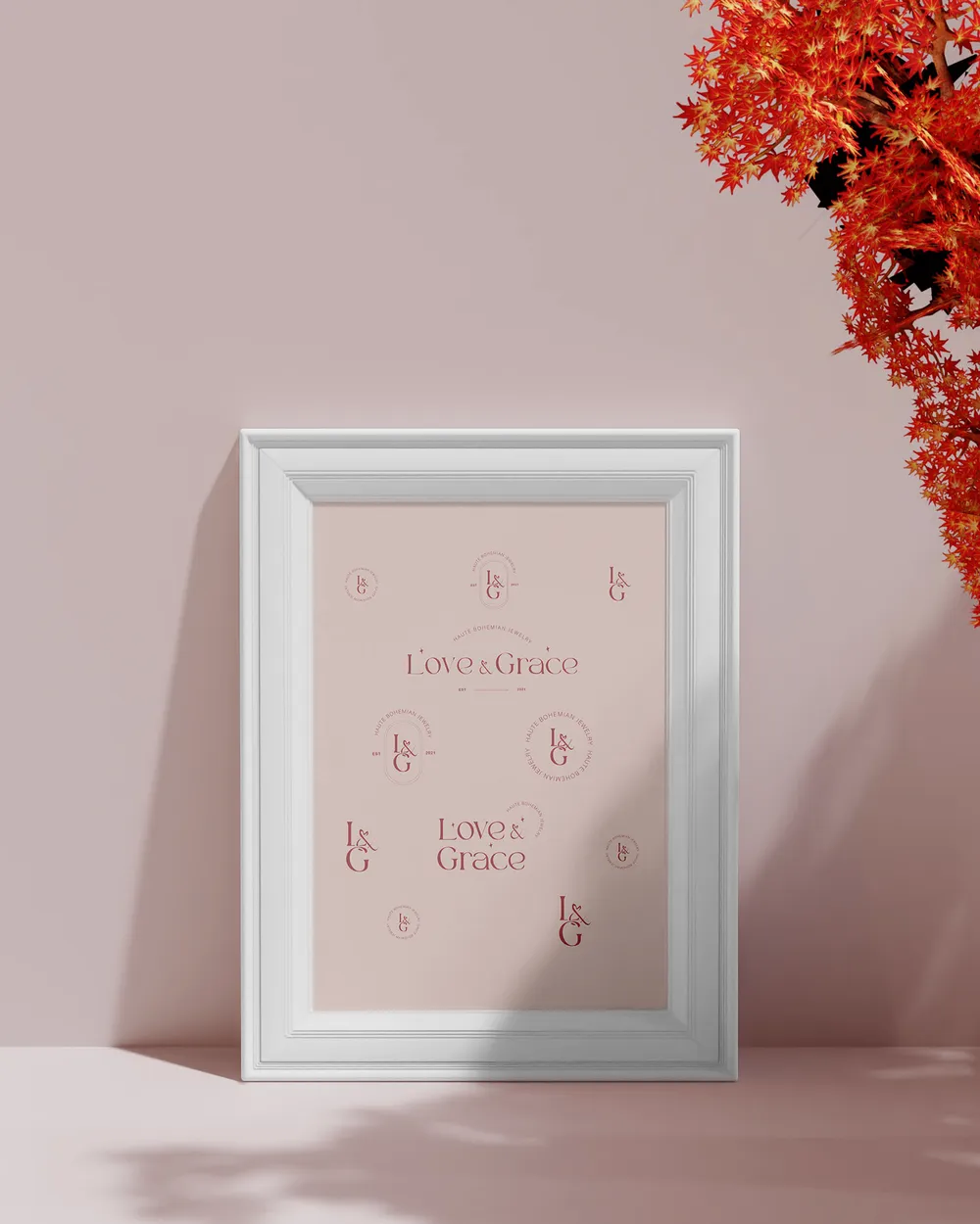 A framed Love & Grace monogram pattern on a pink shelf beside red flowers.