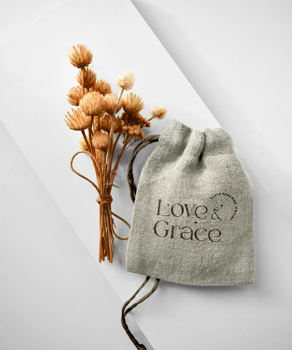 A linen jewelry pouch printed with the Love & Grace logo, tied with dried flowers.