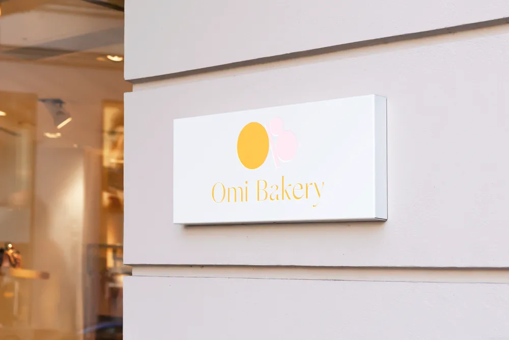 The Omi Bakery logo on a white sign on a shop wall.